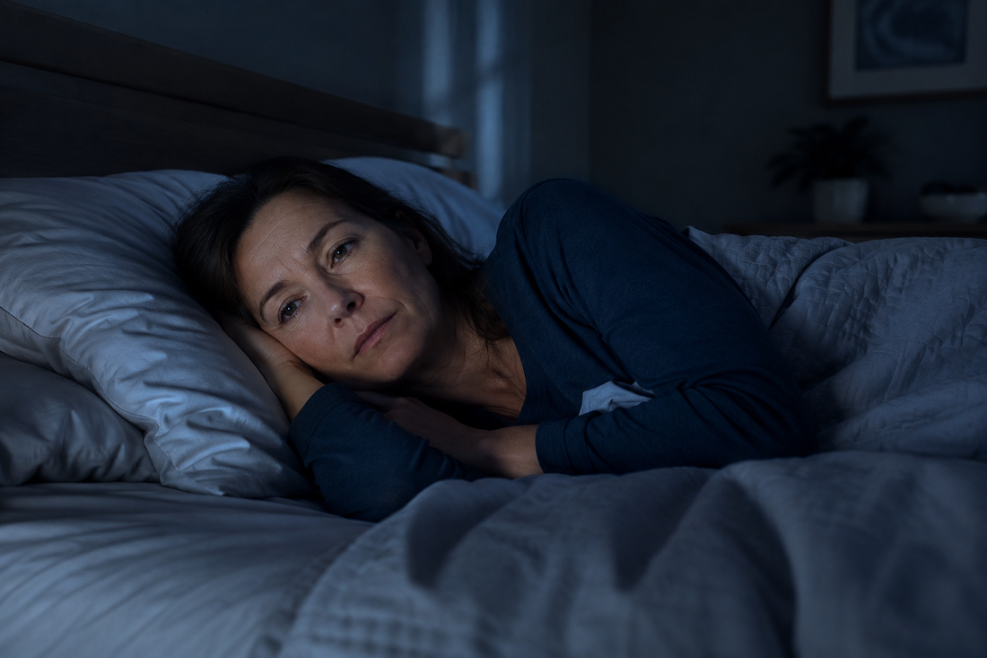 A tired woman lying awake in bed at night in a dark bedroom, showing how poor sleep can make joint pain and stiffness feel worse.