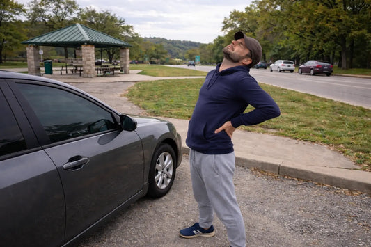 Man stretching his lower back next to his car at a highway rest stop after a long drive