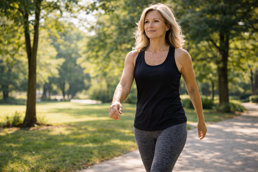 middle-aged woman walking outdoors on a sunny park path wearing gray leggings and a black athletic tank top