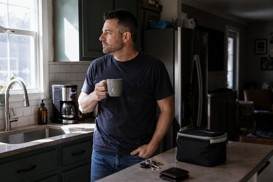 Middle-aged man standing in a kitchen holding coffee in the morning, representing back stiffness and slow movement before a physical work day