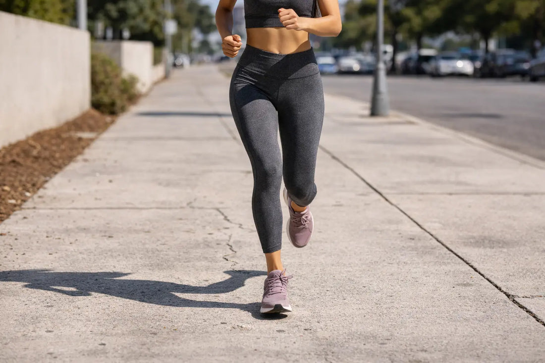 close-up of a female runner’s legs jogging on a cracked sidewalk in harsh midday sunlight, highlighting knee movement and impact
